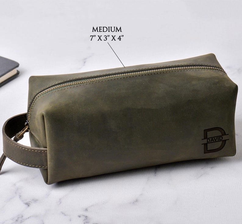 May include: A medium-sized, olive green leather toiletry bag with a zipper closure and a handle. The bag is rectangular, measuring 7" x 3" x 4". The bag has the word "DAVID" and the letter "D" engraved on the front.