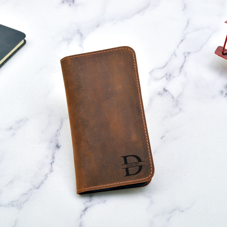 May include: A brown leather wallet with a personalised monogram. The monogram is a capital "D" with the name "DAVID" underneath.
