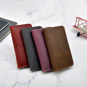 May include: Four leather wallets in different colours: red, black, purple, and brown. The wallets are stacked on top of each other and have a stitched edge.