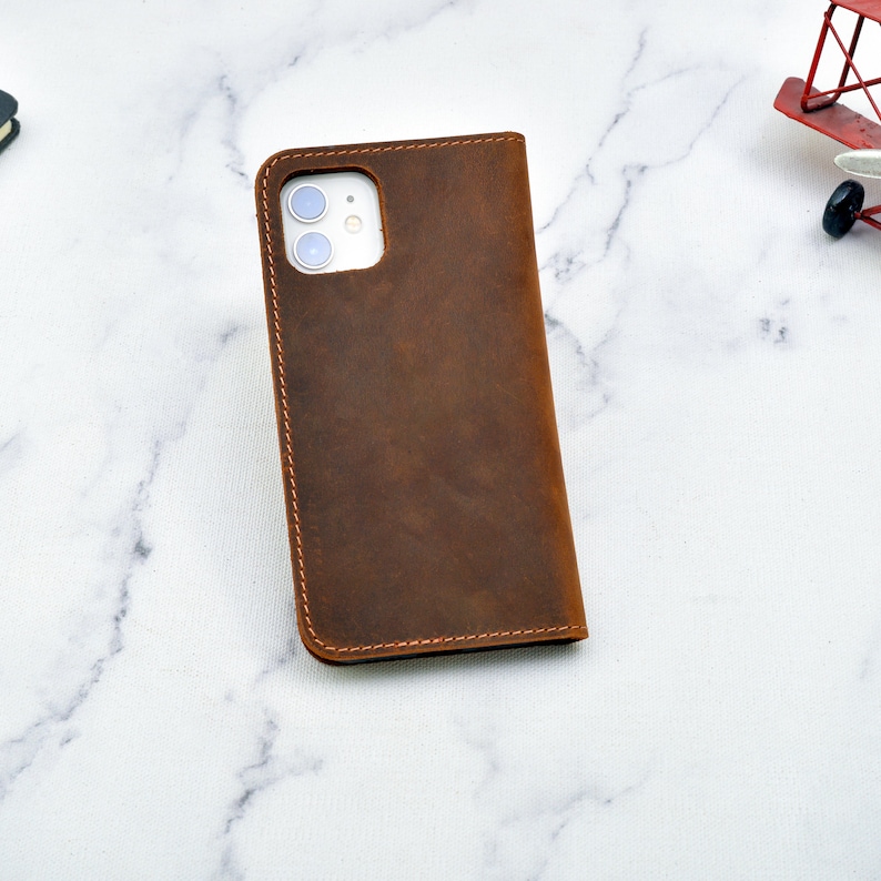 May include: A brown leather phone case with a stitched edge and a cutout for the camera lens.