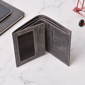 May include: Open grey leather wallet with multiple card slots and a clear ID window. The wallet is displayed open, showcasing its interior design. The wallet is on a white surface.