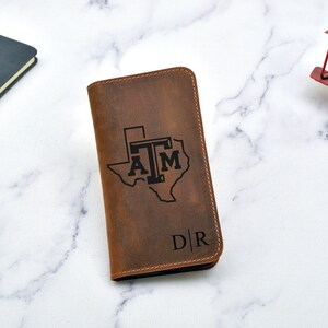 May include: A brown leather wallet with a Texas A&M logo and the initials "D|R" engraved on the front.