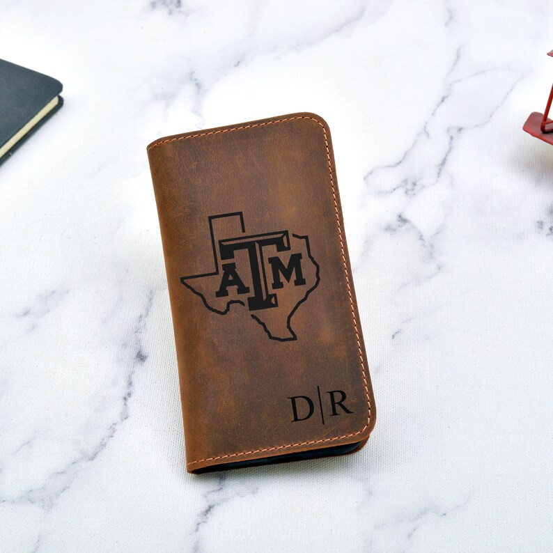 May include: A brown leather wallet with a Texas A&M logo and the initials "D|R" engraved on the front.