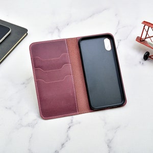 May include: A burgundy leather phone case with a built-in wallet. The case has four card slots and a flap that closes with a snap. The phone case is open and the phone is visible.