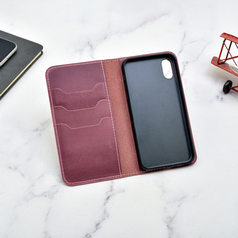 May include: A burgundy leather phone case with a built-in wallet. The case has four card slots and a flap that closes with a snap. The phone case is open and the phone is visible.