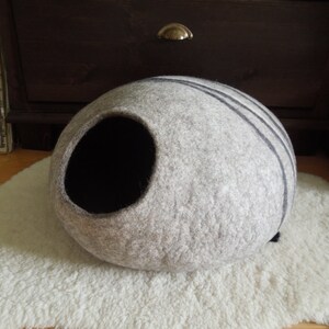 May include: A gray and black felt cat bed shaped like a cave. The bed has a round opening and is made of a soft, fuzzy material.