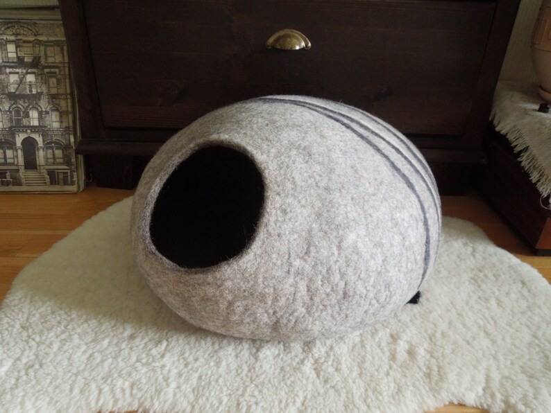 May include: A gray and black felt cat bed shaped like a cave. The bed has a round opening and is made of a soft, fuzzy material.