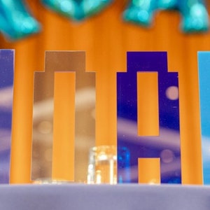 May include: Blue, gold and silver letters spelling out the name "Noah" on a table with clear glass vases.