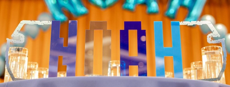 May include: Blue, gold and silver letters spelling out the name "Noah" on a table with clear glass vases.