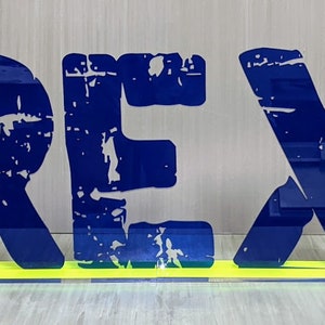 May include: A blue and yellow sign with the word "REX" in large, distressed letters. The sign is flanked by two purple panels with the words "EXTREME" and "RADICAL" written vertically.