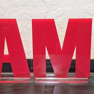 May include: Red acrylic letters spelling out the name "SAM" with a yellow giraffe and black elephant silhouettes behind the letters.