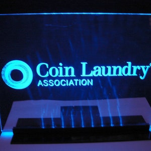 May include: A blue illuminated acrylic sign with the text "Coin Laundry Association" and a circle logo.