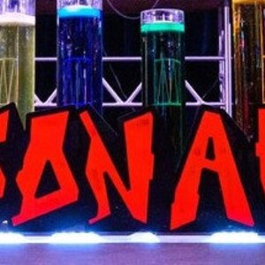 May include: A red and black sign with the name "JONAH" in large, bold letters. The sign is decorated with colourful glass cylinders filled with liquids.