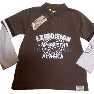 May include: A brown polo shirt with gray sleeves and the text "EXPEDITION POLO EXPLORER ALASKA" in white. The shirt has a collar, buttons, and a tag. The sleeves have navy and white stripes.