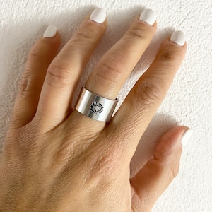 Può includere: Un anello d'argento con un design a forma di cuore. L'anello è largo e ha una superficie testurizzata.