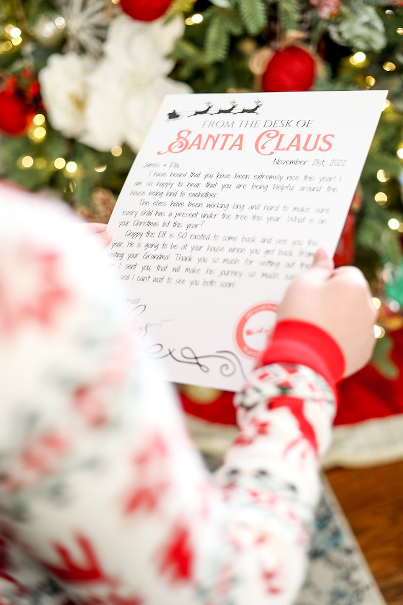 May include: A letter from Santa Claus, dated November 21st, 2022, with a red and black design. The letter is held by a person wearing Christmas pajamas, in front of a decorated Christmas tree.