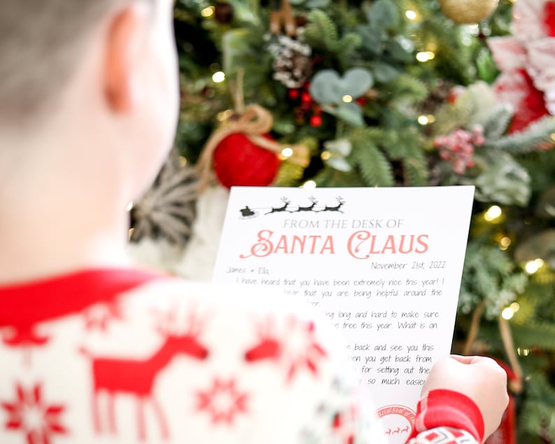 May include: A child in a red and white Christmas sweater reads a letter from Santa Claus. The letterhead reads "FROM THE DESK OF SANTA CLAUS" with a reindeer and sleigh graphic. The letter is dated November 21st, 2022, and is set against a Christmas tree.
