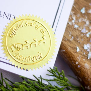 以下が含まれることがあります： 「Official Seal of the North Pole」という文字と、トナカイに引かれたサンタクロースのそりの絵が描かれた金箔のシールです。