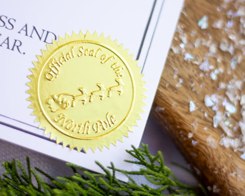 以下が含まれることがあります： 「Official Seal of the North Pole」という文字と、トナカイに引かれたサンタクロースのそりの絵が描かれた金箔のシールです。