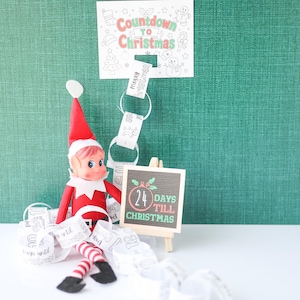 May include: A red and white elf doll sits beside a small wooden easel displaying a sign that reads 24 DAYS TILL CHRISTMAS. Above, a paper sign reads COUNTDOWN TO CHRISTMAS, with a paper chain featuring numbers and holiday illustrations hanging below.