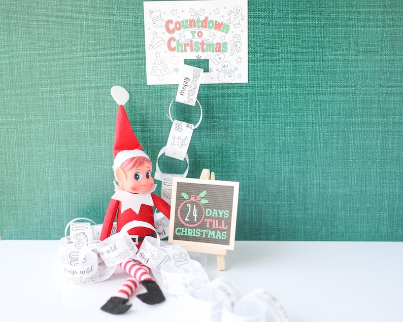 May include: A red and white elf doll sits beside a small wooden easel displaying a sign that reads 24 DAYS TILL CHRISTMAS. Above, a paper sign reads COUNTDOWN TO CHRISTMAS, with a paper chain featuring numbers and holiday illustrations hanging below.