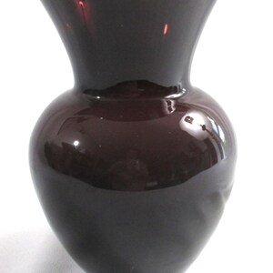 May include: A dark purple glass vase with a wide mouth and a rounded body.
