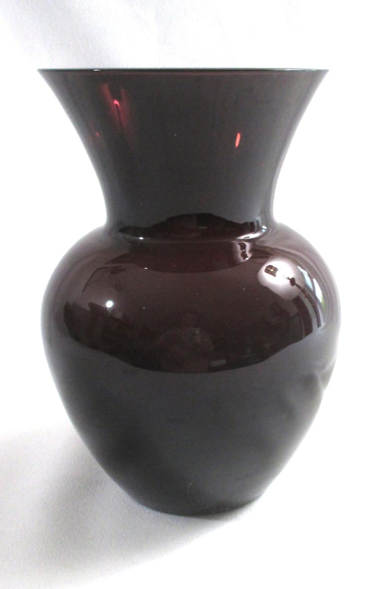 May include: A dark purple glass vase with a wide mouth and a rounded body.