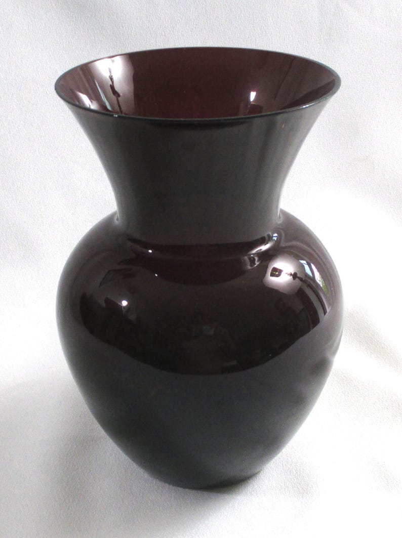 May include: A dark purple glass vase with a wide mouth and a rounded body.