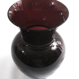 May include: A dark purple glass vase with a wide mouth and a rounded body.