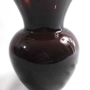 May include: A dark purple glass vase with a wide mouth and a rounded body.