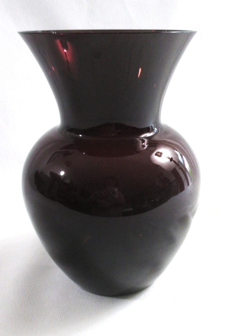 May include: A dark purple glass vase with a wide mouth and a rounded body.