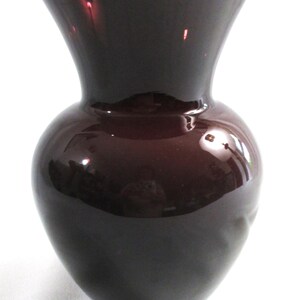 May include: A dark purple glass vase with a wide mouth and a rounded body.