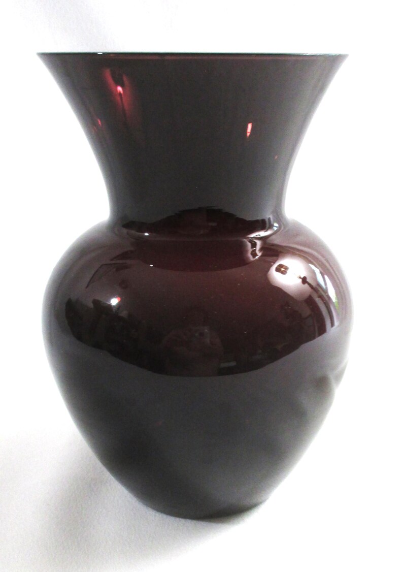 May include: A dark purple glass vase with a wide mouth and a rounded body.