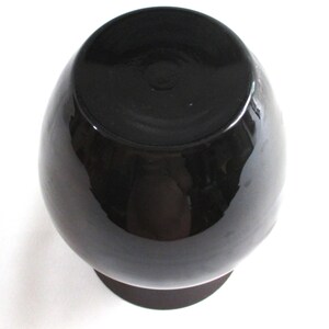May include: A black ceramic vase with a round body and a wide, flat base.