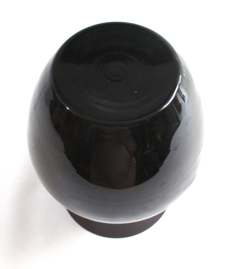 May include: A black ceramic vase with a round body and a wide, flat base.