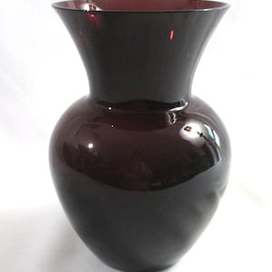 May include: A dark purple glass vase with a rounded body and a flared opening. The vase is smooth and glossy.