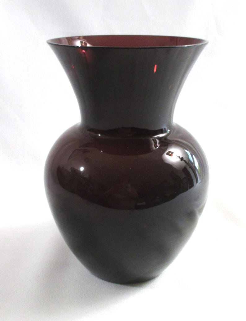 May include: A dark purple glass vase with a rounded body and a flared opening. The vase is smooth and glossy.