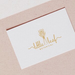May include: A white business card with gold lettering that reads "little leaf botanical". The logo is a stylized drawing of a vase with flowers.