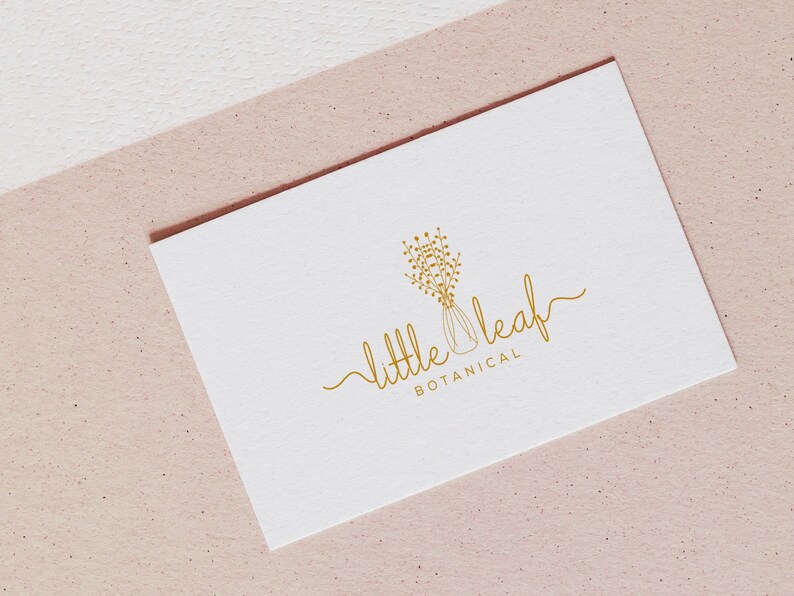 May include: A white business card with gold lettering that reads "little leaf botanical". The logo is a stylized drawing of a vase with flowers.