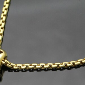 May include: A gold-colored necklace with a unique pendant. The pendant has a rounded shape with cut-out designs and is connected to a box chain. The necklace is made of a shiny, metallic material.