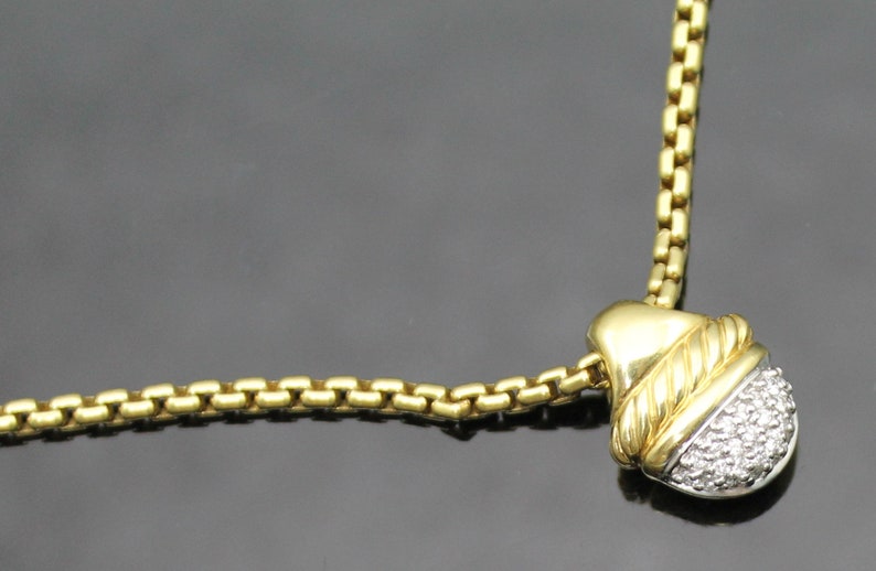 May include: A gold-toned necklace with a pendant featuring a diamond-studded, rounded bottom and a gold top. The pendant is accented with a twisted rope design. The chain is a box chain style.
