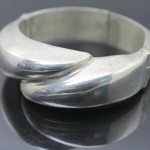 Könnte beinhalten: Ein silbernes Scharnierarmband mit glattem, abgerundetem Design.