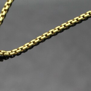 May include: A gold-toned necklace with a pendant featuring a cluster of small, sparkling stones. The pendant has a gold-colored top and a silver-colored bottom. The chain is a box chain style. The necklace is displayed on a dark surface.