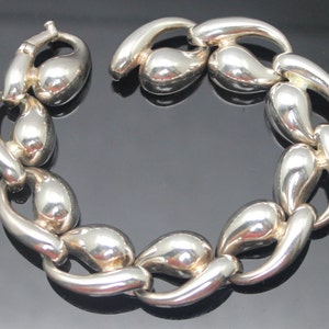 May include: A silver-toned bracelet with a unique chain link design. The links are teardrop-shaped and connected in a continuous loop. The bracelet has a secure clasp for easy wear. The polished metal reflects light, creating a bright, eye-catching accessory.