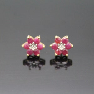 May include: A pair of gold flower-shaped earrings with red ruby and white diamond accents.