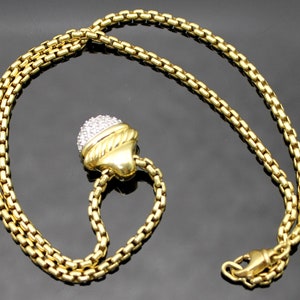May include: A gold-toned necklace with a round pendant encrusted with small, clear stones. The pendant is attached to a chain with a lobster clasp. The necklace is displayed on a dark surface.