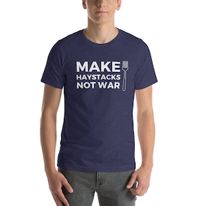 Peut inclure: T-shirt bleu marine avec le texte blanc "MAKE HAYSTACKS NOT WAR" et un dessin de fourchette. Le t-shirt est à col rond et à manches courtes.