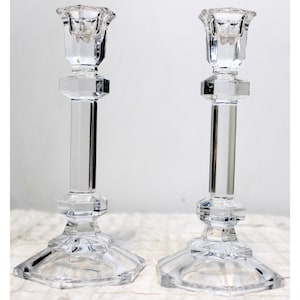 May include: Two clear glass candle holders with a geometric design. The holders have a square base and a round top.