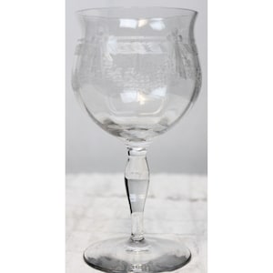 May include: A clear glass wine glass with an etched design of grapes and vines. The glass has a tall stem and a wide bowl.