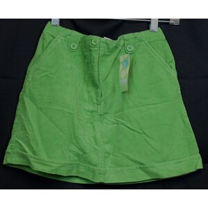 May include: A bright green corduroy skirt with two front pockets and three button closures. The skirt has a straight hemline and a small tag attached to the waistband. The fabric has a ribbed texture.